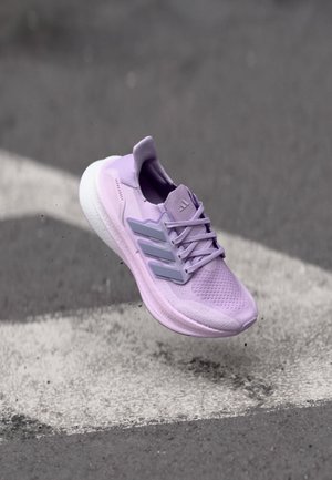 Lila Sportschuh mit atmungsaktivem Mesh-Obermaterial, drei grauen Akzenten, einer gepolsterten Sohle und Schnürsystem, in der Luft über einer markierten Oberfläche.