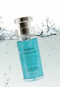 Przezroczysta szklana butelka serum z srebrną zakrętką, zawierająca jasnoniebieski płyn. Tekst zawiera "Kolagen Morski" i "Eclat Skin London." Woda rozpryskuje się wokół.