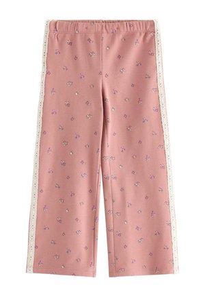 Ung pige smiler med armene udstrakte iført en pink sweatshirt med blomsterprint og matchende bukser med hvide blonde detaljer.