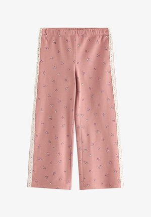 Ung pige smiler med armene udstrakte iført en pink sweatshirt med blomsterprint og matchende bukser med hvide blonde detaljer.