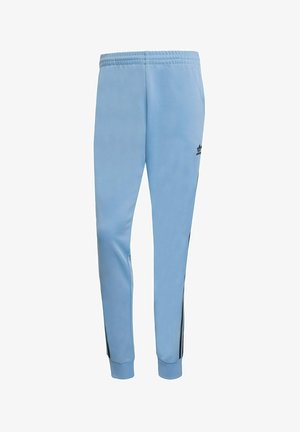 Pantaloni jogger azzurri chiari realizzati in tessuto liscio, con una vita elastica e strisce laterali nere. Logo Adidas in nero sulla gamba sinistra.