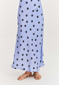 Svetlomodré maxi šaty s čiernou kvetinovou potlačou, hladká tkanina, mierny lesk, bočný rozparok, skombinované s svetlohnedými sandálmi so zapletenými popruhmi.