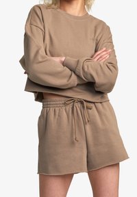 Felpa corta marrone con maniche lunghe e colletto rotondo, abbinata a pantaloni corti con coulisse dello stesso colore, entrambi realizzati in un tessuto morbido.