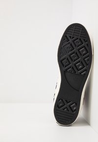 Suela de zapato de goma negra con un diseño texturizado de patrón en diamante y borde blanco. Presenta la marca "Converse All-Star".