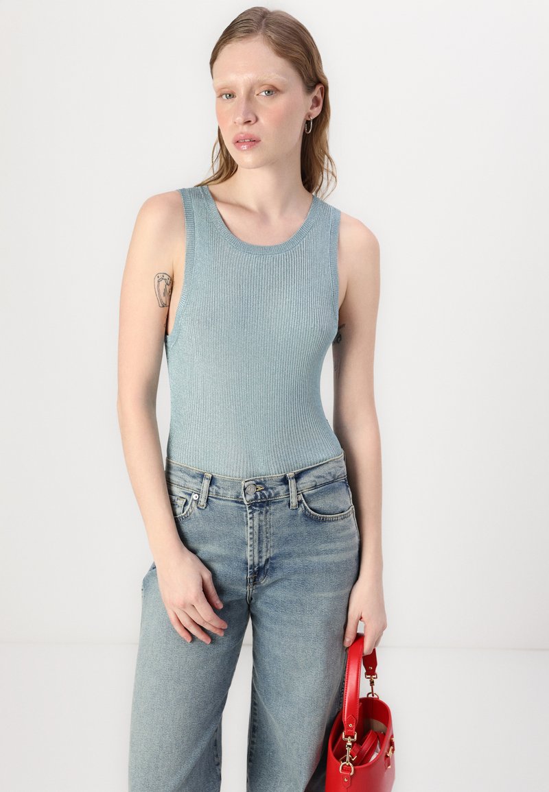 Jasnoniebieski ribbed top bez rękawów z okrągłym dekoltem w połączeniu z jasnoniebieskimi dżinsami z wysokim stanem. Czerwona torebka na ramię.