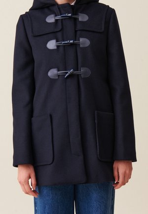 Abrigo tipo toggle azul marino con capucha, tres cierres negros, dos grandes bolsillos delanteros, llevado sobre vaqueros azules.
