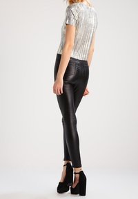 Haut à manches courtes argenté et à rayures, associé à des leggings noirs brillants taille haute et des sandales à talons épais noires. Vue arrière présentée.