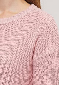 Pull rose en tricot avec un col rond, un tissu texturé et une coupe ample avec épaules tombantes.