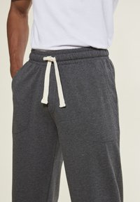Graue Sweatpants mit einer weichen Textur, elastischem Bund und weißem Kordelzug. Verfügt über seitliche Taschen und ein lässiges Design.