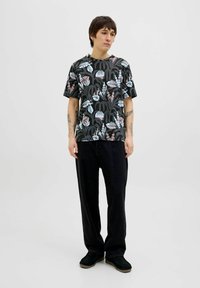 Tricou negru cu un model floral și de plante în culori pastelate, asortat cu pantaloni negri largi și încălțăminte închise.
