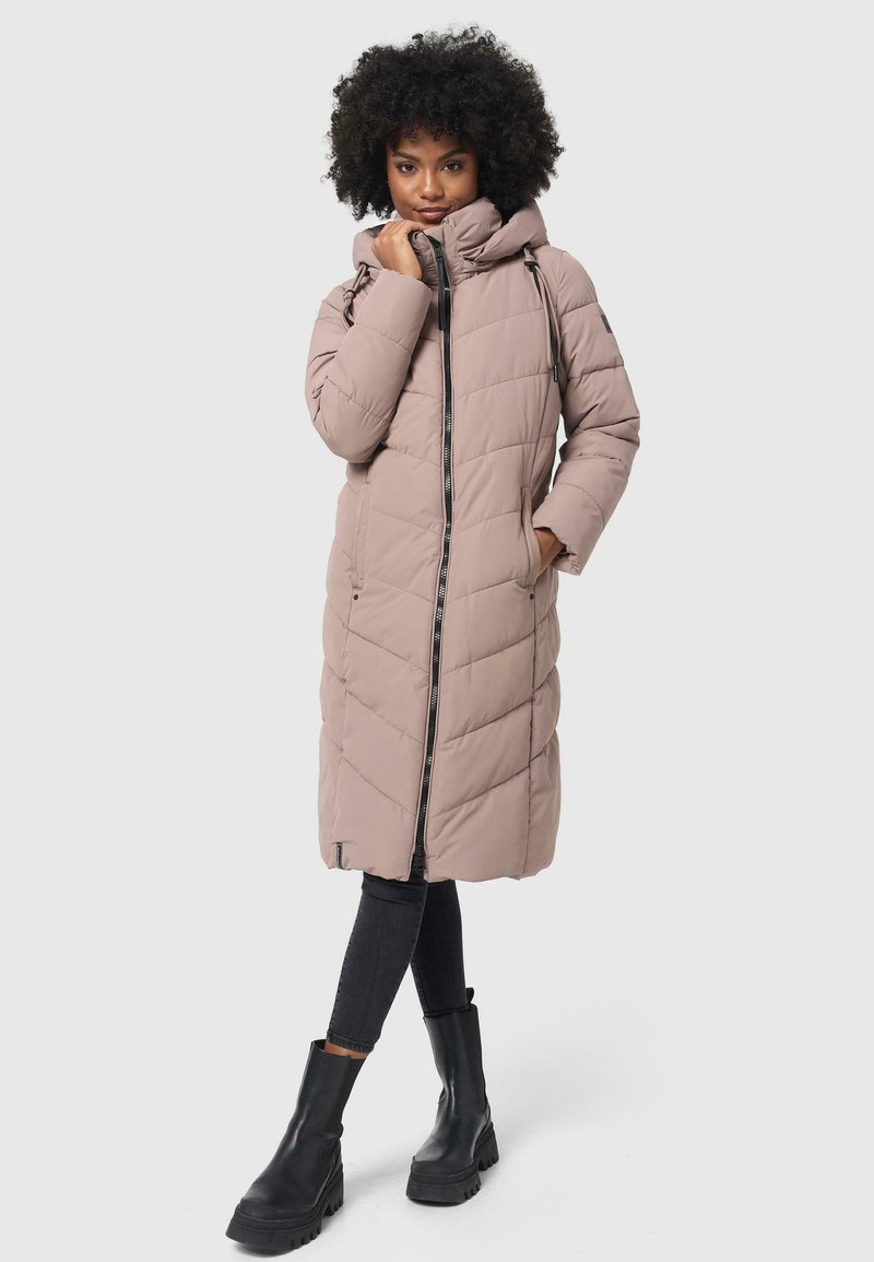 Long beige puffer coat with a hood, featuring a front zipper, side pockets, and diamond quilted pattern. Worn over dark jeans and chunky black boots.