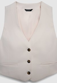 Gilet de couleur crème avec un décolleté en V, quatre boutons marron et deux poches plates à l'avant. Fabriqué en tissu texturé.