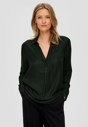 Ciemnozielona bluzka w wzór houndstooth, z długimi rękawami, kołnierzykiem i luźnym krojem, w zestawieniu z ciemnymi spodniami.