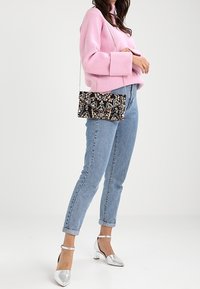 Černá crossbody kabelka s květinovým vzorem a řetízkovým popruhem; obdélníkový tvar s chlopní ve stylu obálky. Nošená s lehkými džínami a stříbrnými podpatky.