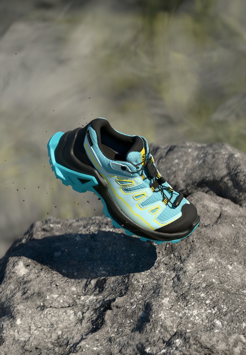 Scarpa da trail running blu e nera con tomaia in mesh testurizzato, dettagli gialli e suola robusta progettata per garantire aderenza su superfici rocciose.