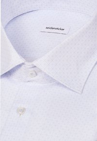 Chemise blanche avec un motif géométrique subtil, col boutonné et étiquette de marque visible indiquant "seidensticker."