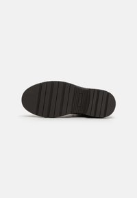 Suela de zapato de goma negra con surcos y estrías horizontales para tracción, que presenta una forma suave y redondeada y un área de talón reforzada.