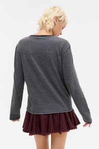 Dlhý prúžkovaný top v šedej a čiernej farbe, doplnený bordovou kockovanou sukňou s plisovaným dizajnom a strapcami na okraji.