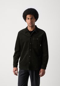 Camisa chaqueta de pana negra con botones al frente, cuello puntiagudo y un único bolsillo en el pecho. Tejido texturizado con un acabado suave.