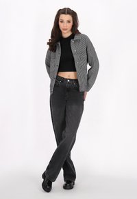 Svartvit randig jacka över en svart crop top, parat med högmidjade svarta jeans och svarta skor. Släta texturer och avslappnad passform.