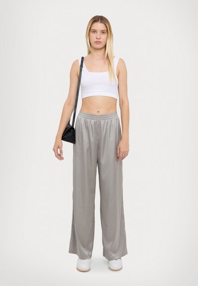 Witte crop top en grijze wijde broek van gladde stof. Het model draagt een kleine zwarte tas en witte sneakers. Eenvoudige, casual outfit.