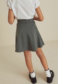 Grijze uitlopende rok van zachte stof, met een gladde tailleband. Complementair met zwarte schoenen en witte sokken met een lichte rimpel.