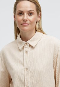 Beige Baumwollhemd aus Cord mit durchgängiger Knopfleiste, spitzem Kragen und geripptem Muster. Die Knöpfe sind in einem passenden hellen Farbton.