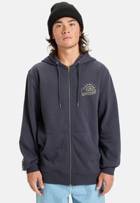 Navy zip-up hoodie made of cotton blend, featuring a drawstring hood, front pockets, and gold logo design on the left chest.
