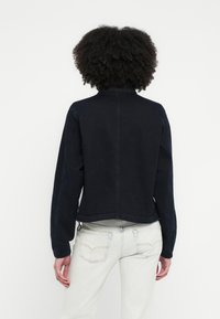 Σκούρο μπλ�ε μπουφάν από τζιν με όρθιο γιακά, ελαστικά μανίκια και άνετη εφαρμογή. Διαθέτει εμφανείς ραφές και cropped σχεδιασμό.