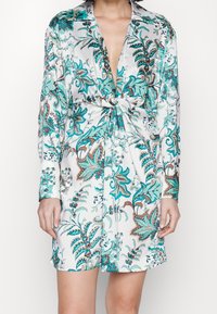 Sukienka koszulowa z jedwabiu z kwiatowym wzorem w turkusowych i brązowych odcieniach, z głębokim dekoltem w kształcie litery V i węzłem z przodu. Długie rękawy.