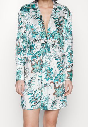 Zijden shirtjurk met een bloemenpatroon in turquoise en bruine tinten, met een diepe V-hals en een geknoopt detail aan de voorkant. Lange mouwen.