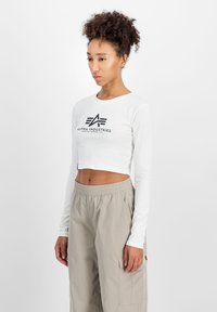Hvit langermet crop-top med svart logo-print. Kombinert med lysegrå, løstsittende cargo-bukser med elastisk linning.