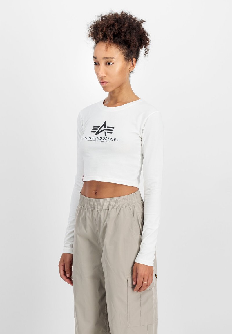 Hvit langermet crop-top med svart logo-print. Kombinert med lysegrå, løstsittende cargo-bukser med elastisk linning.