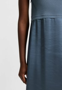 Sleeveless dress with a fitted knit top in slate blue and a flowy, shiny fabric skirt. Smooth texture and subtle sheen.