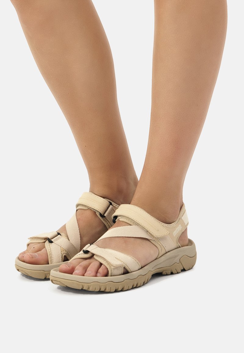 Beige justerbare sandaler med kryssremmer, polstret fotseng og strukturert gummisåle. Designet for komfort og utendørs bruk.