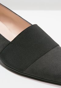 Chaussure plate pointue en daim noir avec une large bande élastique sur le dessus et une doublure intérieure beige douce.