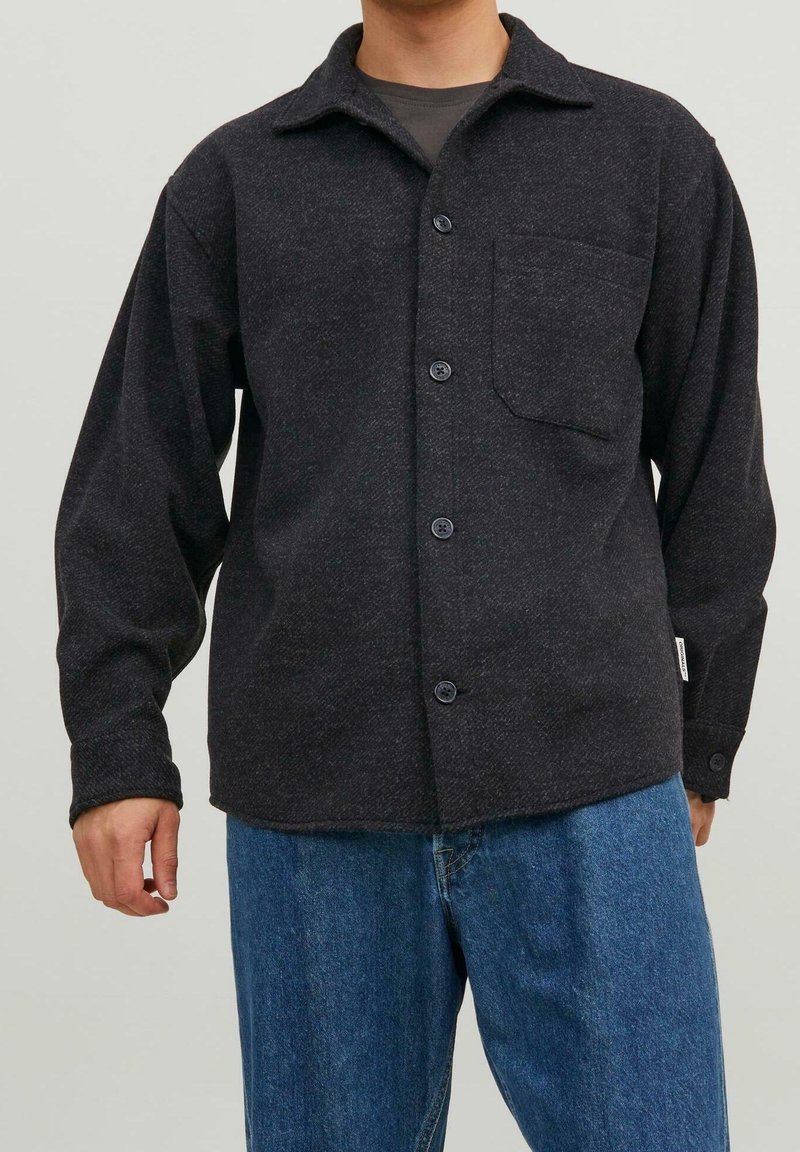 Camicia grigio scuro con bottoni, realizzata in tessuto testurizzato, con tasca sul fronte, colletto a risvolto e maniche lunghe, abbinata a pantaloni in denim blu.