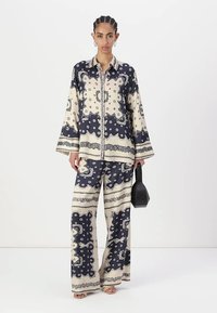 Completo a due pezzi con camicia a fantasia e pantaloni a gamba larga in crema e blu navy. Il tessuto ha una consistenza liscia con un motivo floreale.