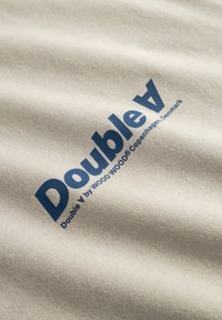 Lysebeige stof med en glat tekstur og blå tekst, der lyder "Double A" og "Double A by WOOD WOOD København, Danmark."