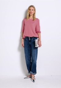 Top rosa a maniche lunghe e dalla vestibilità ampia abbinato a jeans scuri a vita alta. Borsa argento e ballerine argentate lucide completano l'outfit.