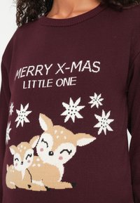 Vínový sveter s pletenou grafikou dvoch srnčiat, bielym textom "MERRY X-MAS LITTLE ONE" a bielymi vzormi vločiek.