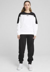 Valge Puma kapuutsiga sweatshirt mustade õlavarre aktsentide ja logoga, kombineeritud mustade spordipükstega, millel on valged külgtriibud ja logo. Kerge kangas.