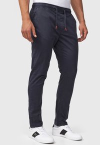 Navy cotton joggers with a tapered fit, elastic waistband, drawstring, and subtle side pockets, paired with white sneakers with black accents.