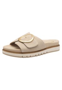 Sandale beige à enfiler avec une large sangle, une grande boucle circulaire dorée, une semelle rembourrée et une semelle extérieure blanche texturée.