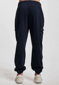 Pantaloni della tuta blu navy con pannello laterale testurizzato, vita elasticizzata e caviglie a costine. Presentano due tasche laterali per il deposito.