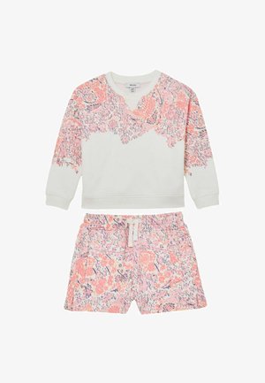 Ilgas rankovėmis baltas džemperis su rausvu gėlėtų raštų įspaudimu viršuje ir rožiniais gėlėtais šortais su raišteliu juosmens srityje.