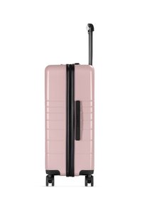 Valigia rigida rosa con zip nera, superficie testurizzata, manico retrattile e quattro ruote per la mobilità. Etichetta del marchio sul lato.
