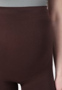 Brown high-waisted leggings made of stretchy fabric, featuring a smooth texture and seamless design, shown at waist level.