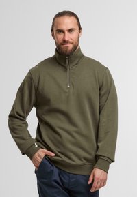 Felpa verde oliva con collo alto e zip a metà. Presenta maniche lunghe e una vestibilità rilassata. Texture morbida e liscia.