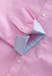 Camicia da uomo rosa chiaro realizzata in tessuto testurizzato. Presenta un collo foderato a strisce blu e bianche e bottoni bianchi.